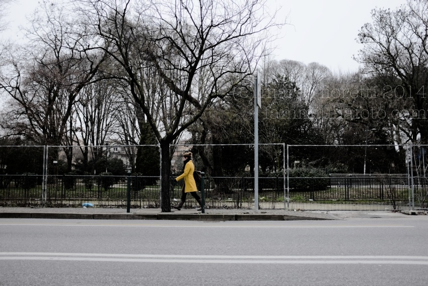 Ragazza con cappotto giallo che cammina sul marciapiede lungo il parco